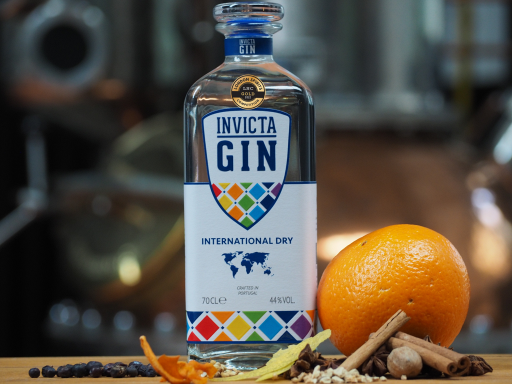 A bottle of international dry Invicta Gin with an alcohol competition gold medal, with ingredients on the ground
