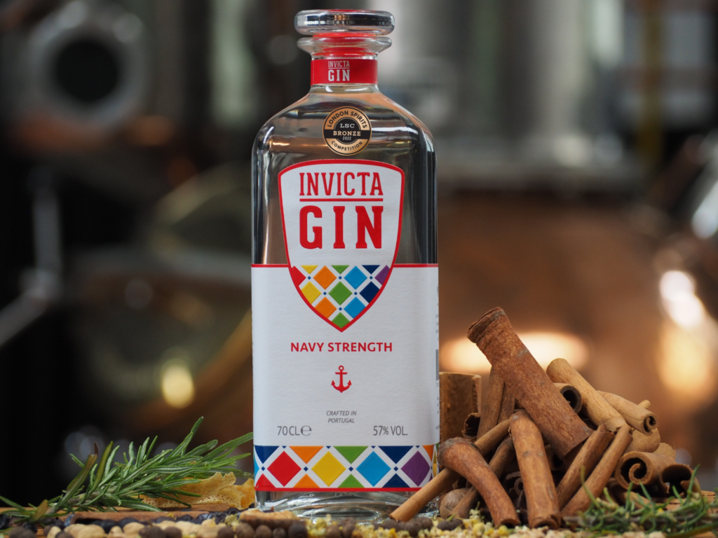 A bottle of Navy Strength Invicta Gin with an alcohol competition bronze medal, with ingredients on the ground