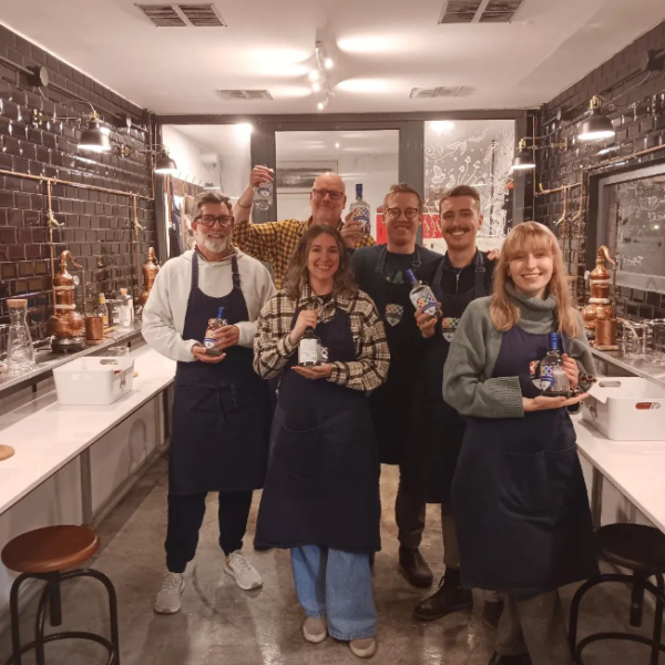 six gin school students standing in front of a Gin School room holding bottles of the gin they made