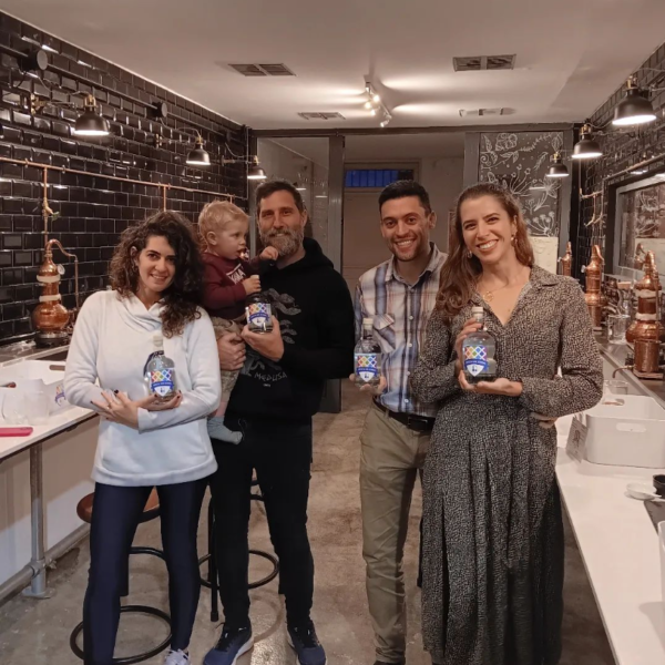 four gin school students and a toddler standing in front of a Gin School room holding bottles of the gin they made