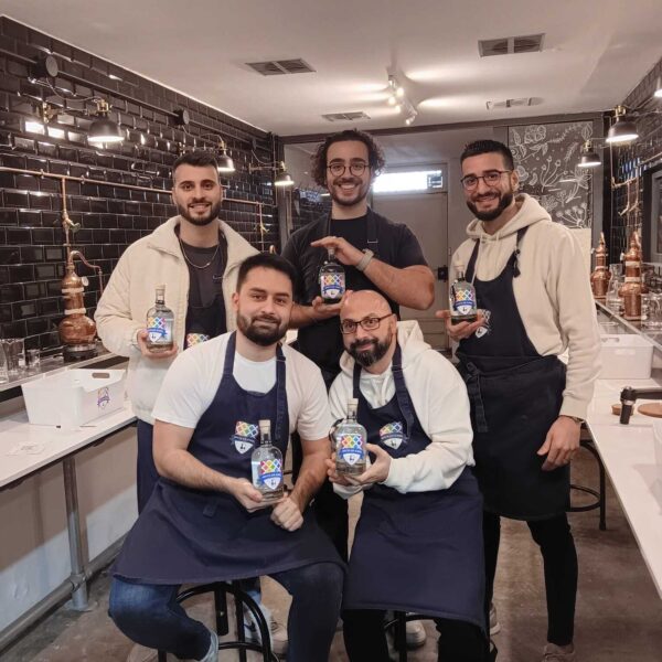 five gin school students standing in front of a Gin School classroom holding bottles of the gin they made