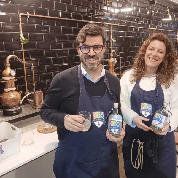 two gin school students standing in front of a Gin School classroom holding bottles of the gin they made