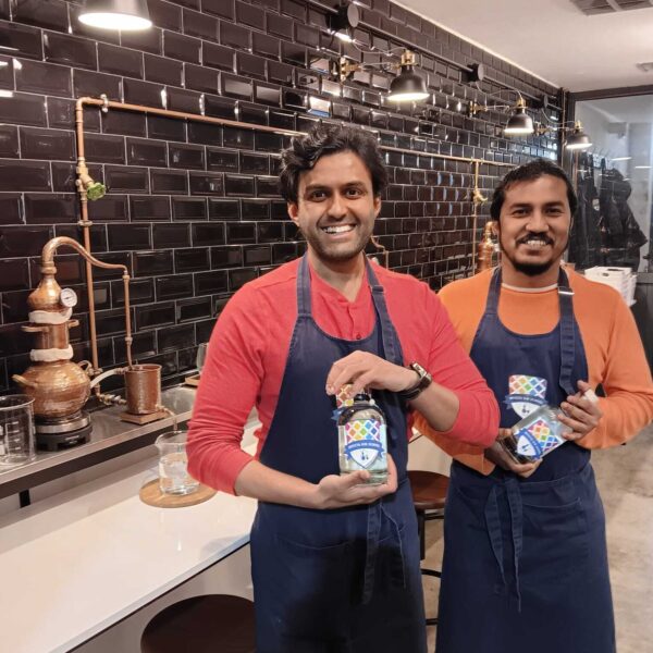 two gin school students standing in front of a Gin School classroom holding bottles of the gin they made