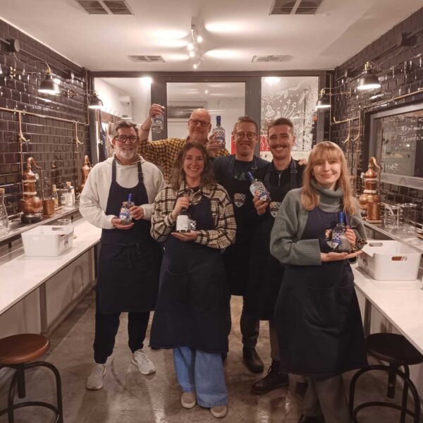 six gin school students standing in front of a Gin School classroom holding bottles of the gin they made