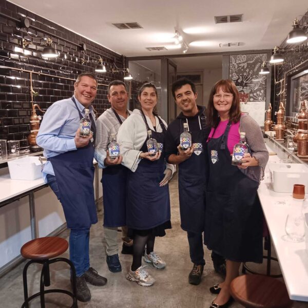 five gin school students standing in front of a Gin School classroom holding bottles of the gin they made