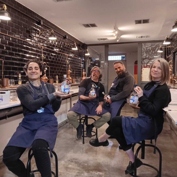 four gin school students standing in front of a Gin School classroom holding bottles of the gin they made