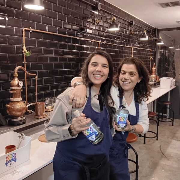 two gin school students standing in front of a Gin School room holding bottles of the gin they made
