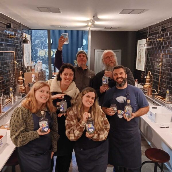 six gin school students standing in front of a Gin School classroom holding bottles of the gin they made